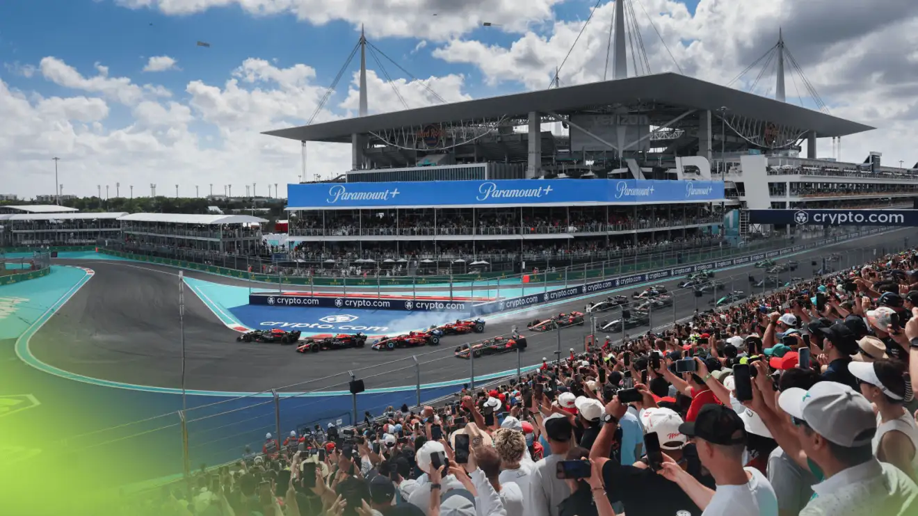 c-103 The F1 cars navigate the first corner at the 2024 Miami Grand Prix as fans watch from the grandstands with the stadium in the background