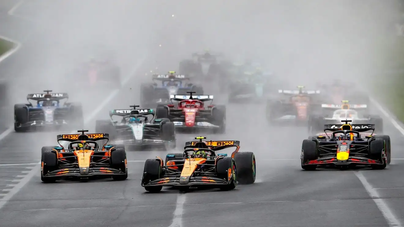 c-1532 Lando Norris leads the pack as it races towards Turn 1 in the rain at Albert Park at the start of the 2025 Australian Grand Prix.