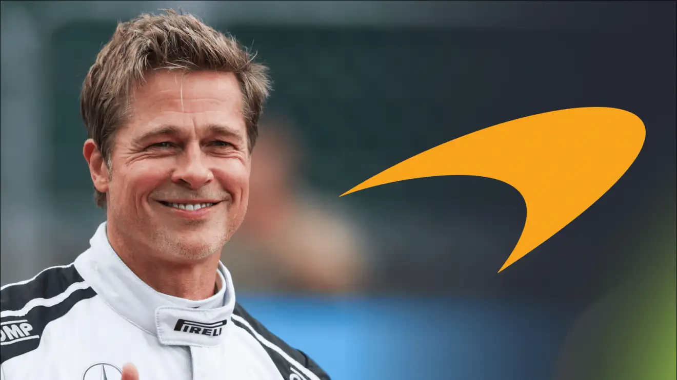 c-1075 Brad Pitt smiles while wearing racing overalls with an orange McLaren logo alongside him